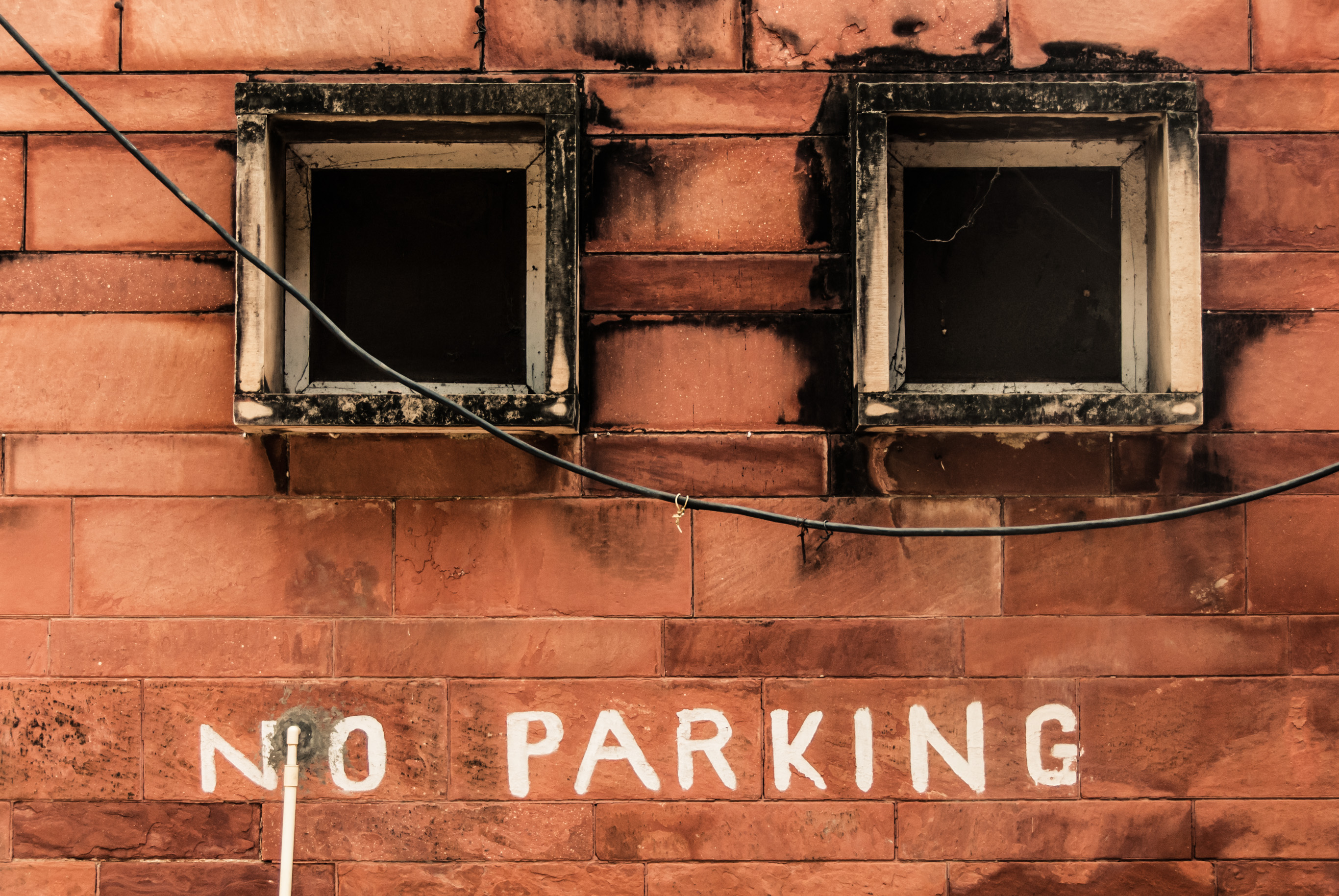 Deux petites fenêtres dans un mur de grès rouge, « NO PARKING » peint en dessous