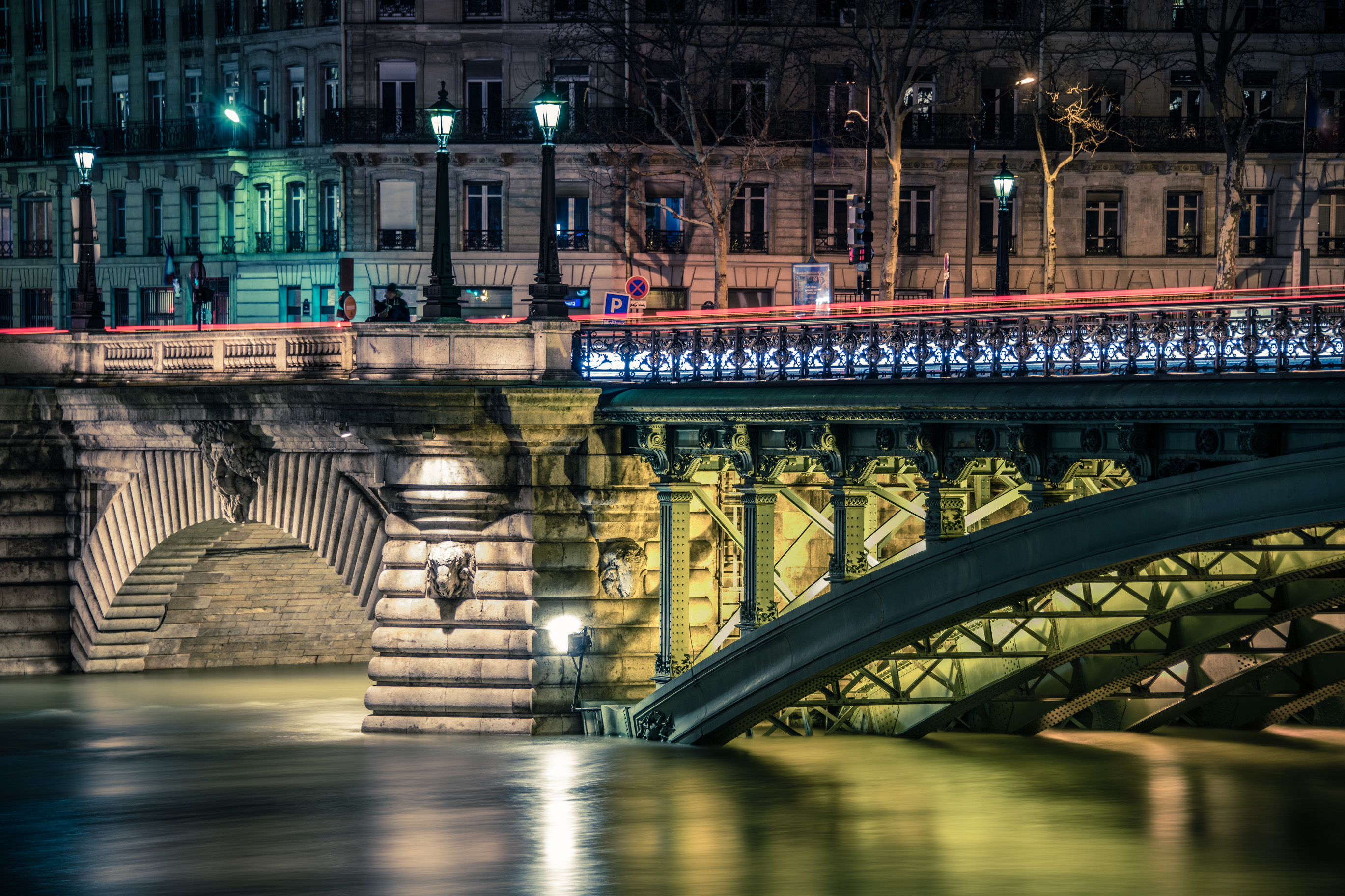 Un pont de pierre et un pont métallique éclairés de nuit au-dessus de l'eau