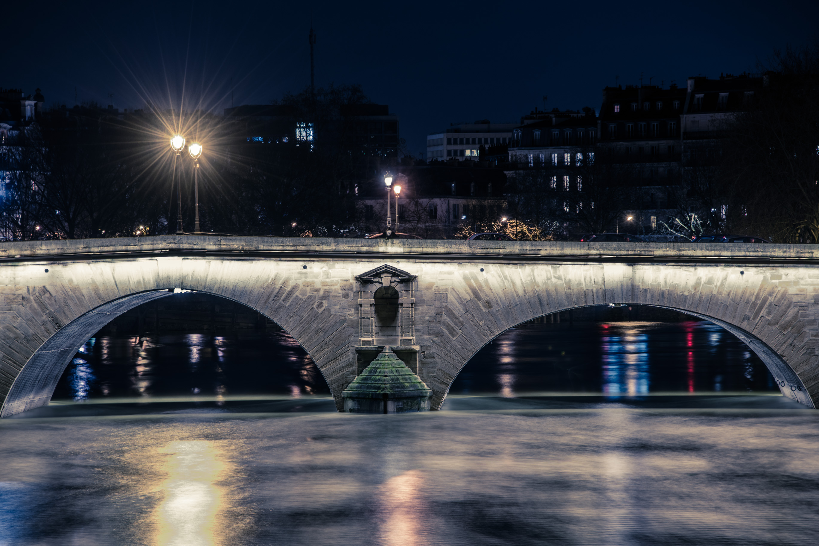 Un pont de pierre à deux arches éclairé de nuit, ses reflets sur l'eau