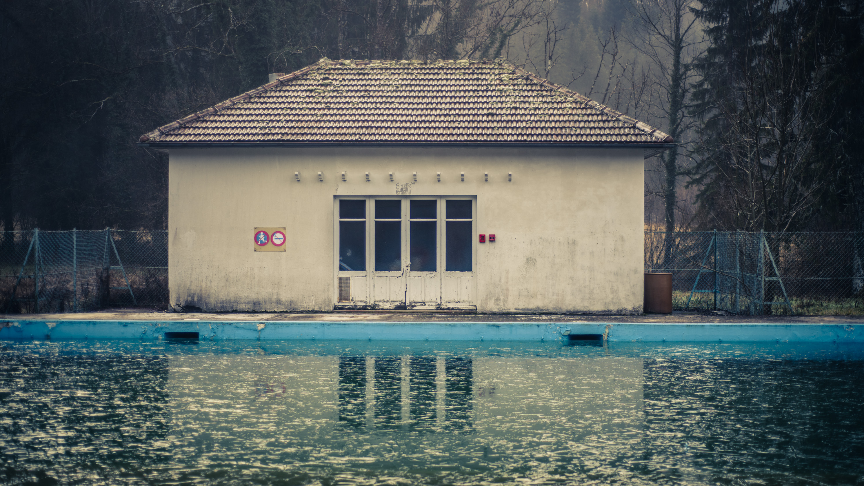 Un pavillon au bord d'une piscine vide de baigneurs, son reflet dans l'eau