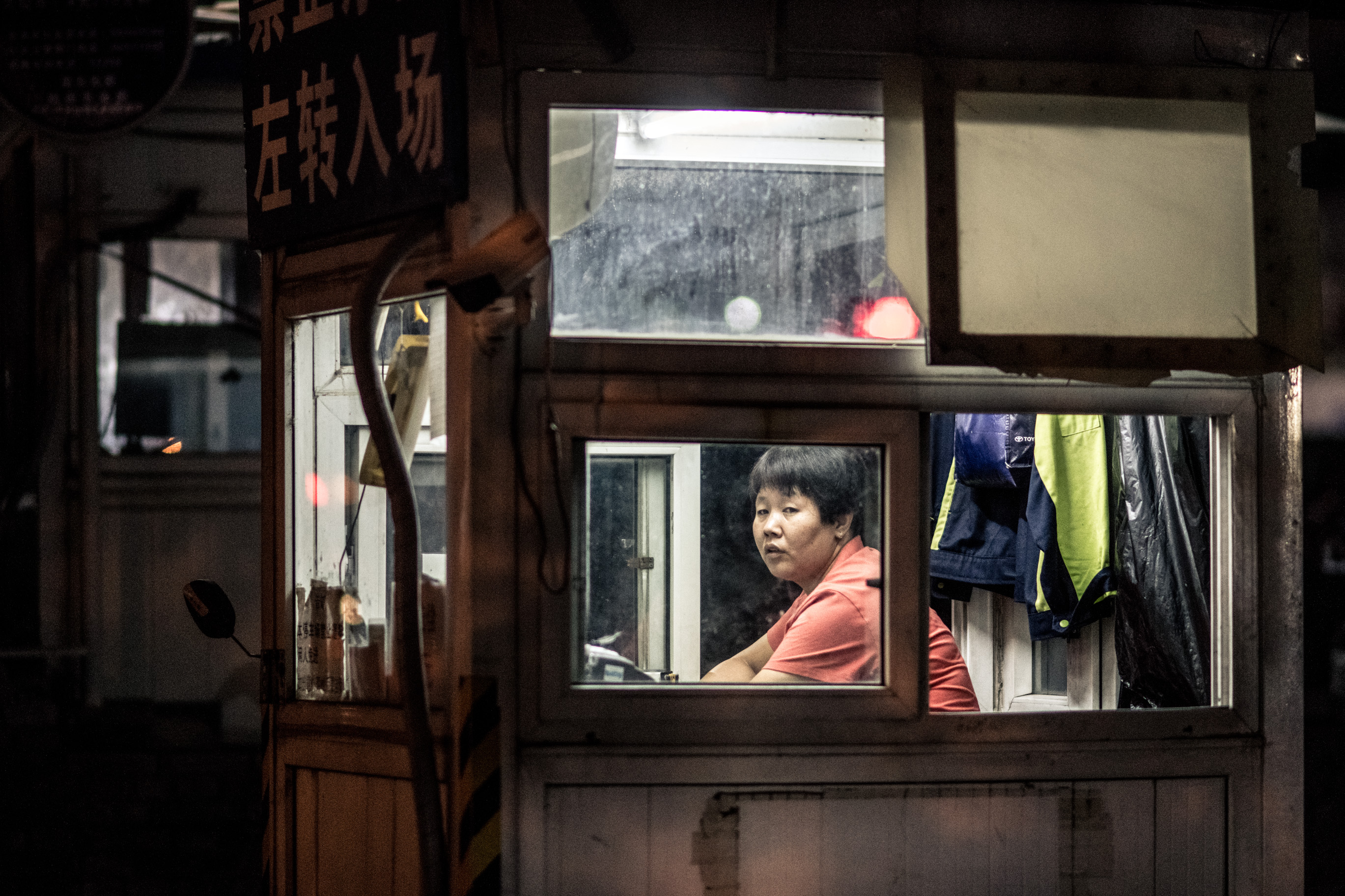 Une femme à la fenêtre d'un poste de garde, sous un panneau en caractères chinois