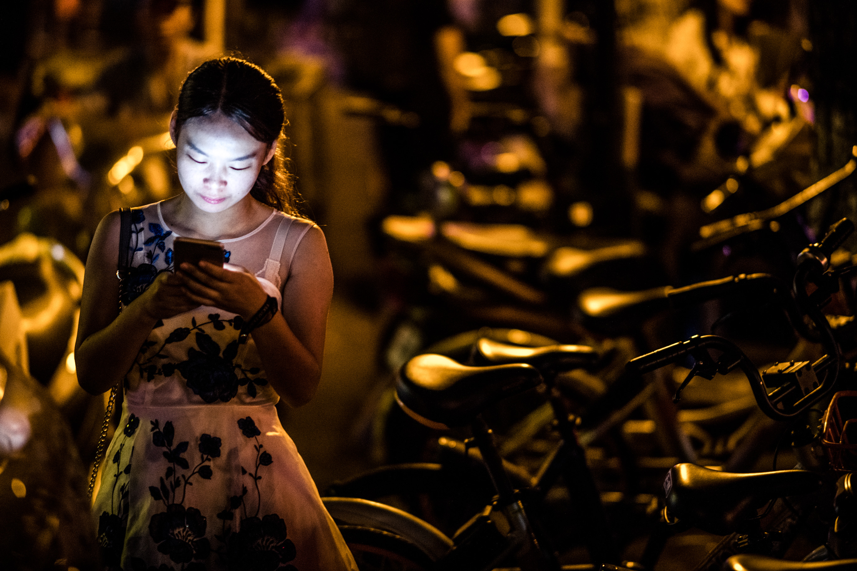Une jeune femme éclairée par l'écran de son téléphone, devant des vélos empilés dans la pénombre