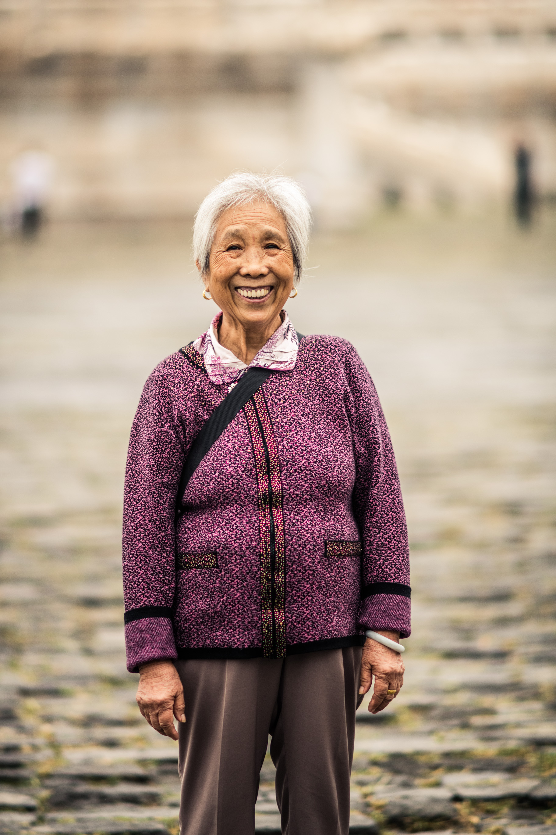 Portrait d'une femme âgée souriante, en gilet violet, sur un dallage